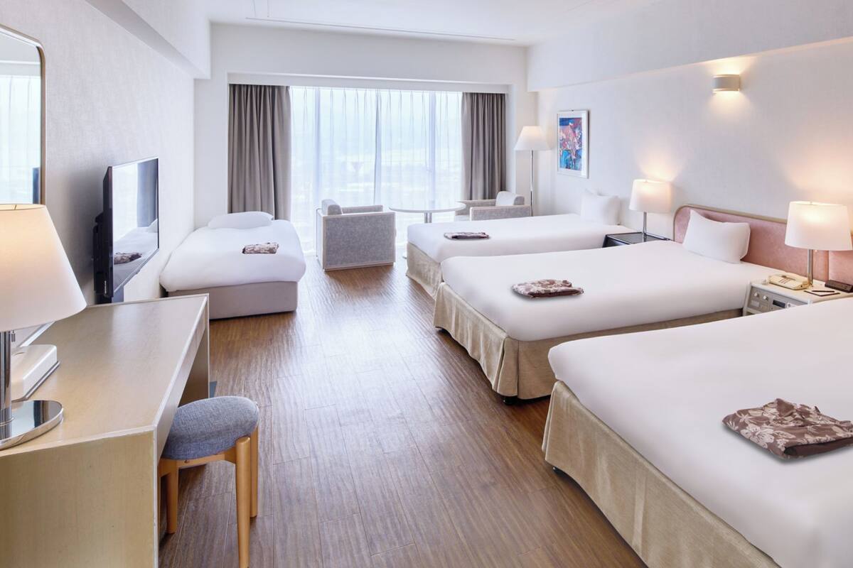 A hotel room with two beds, a desk, a chair, a TV, and a window with curtains.