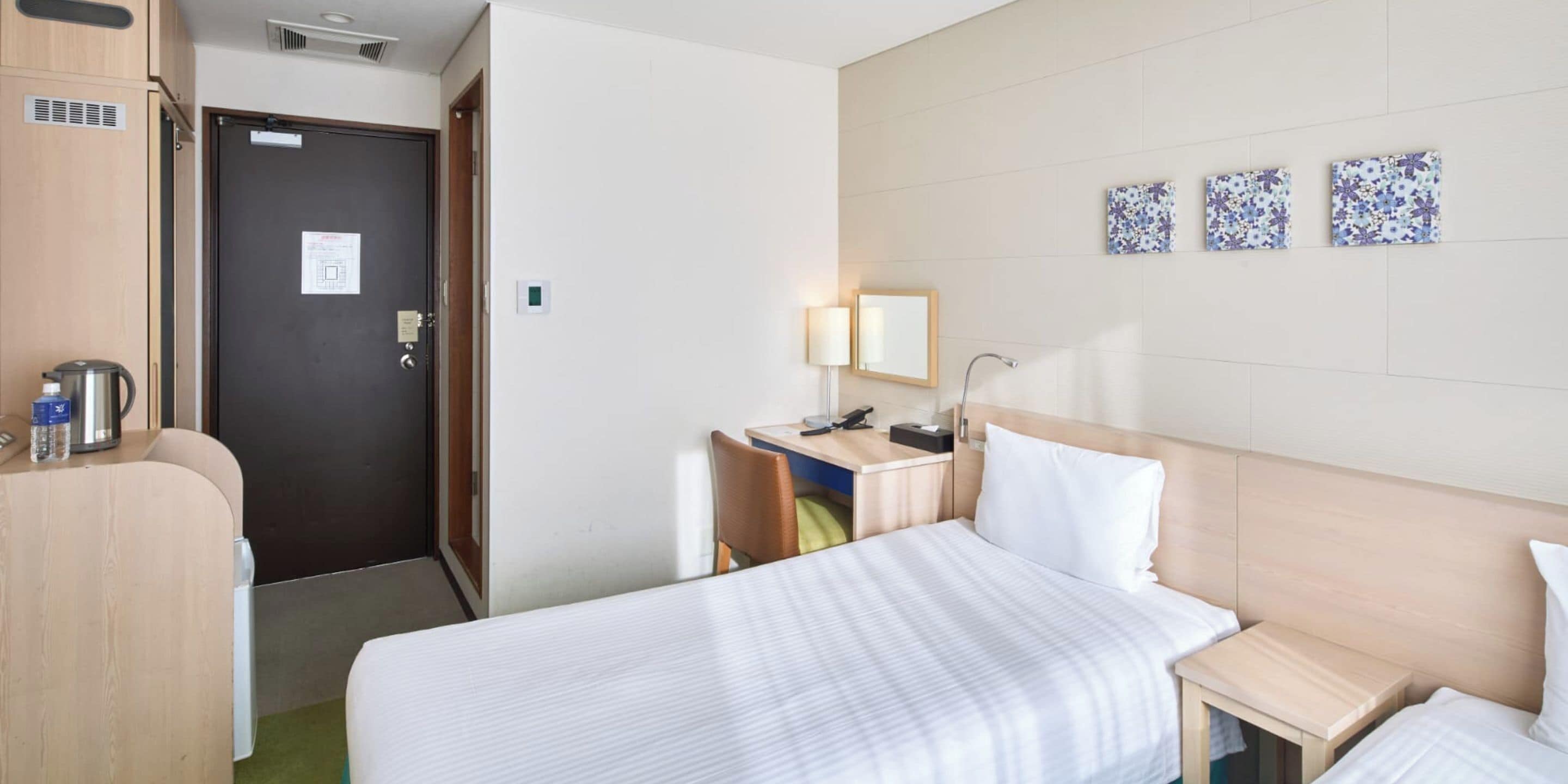 Quarto de hotel com cama, escrivaninha, cadeira, luminária e cafeteira.