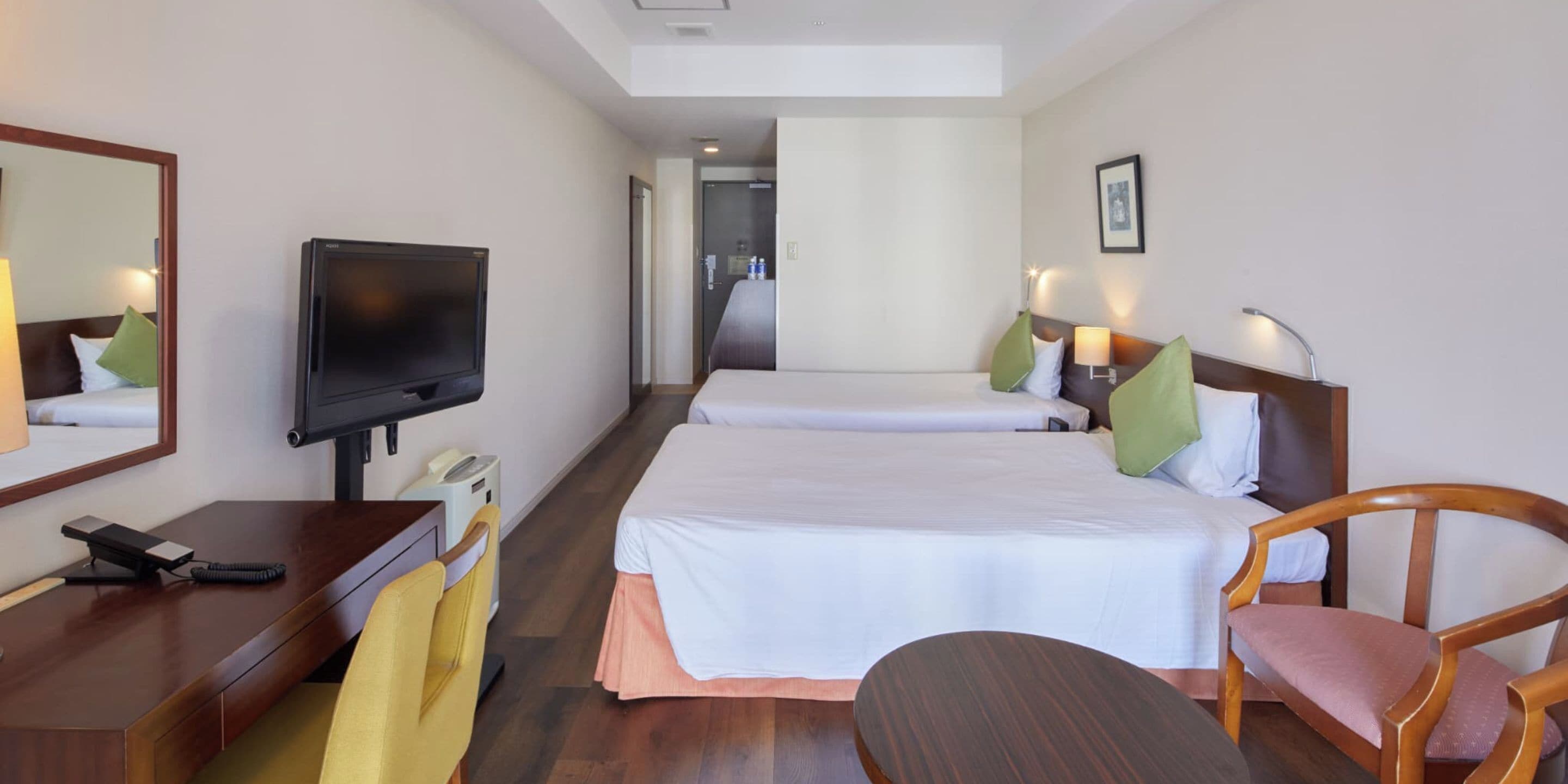 Una habitación de hotel con una cama, un escritorio con televisor, una silla y una mesita de noche.