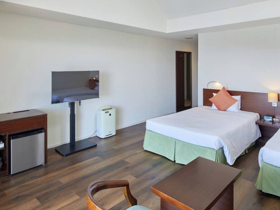 Habitación de hotel con escritorio, dos camas, televisión y una pequeña kitchenette.