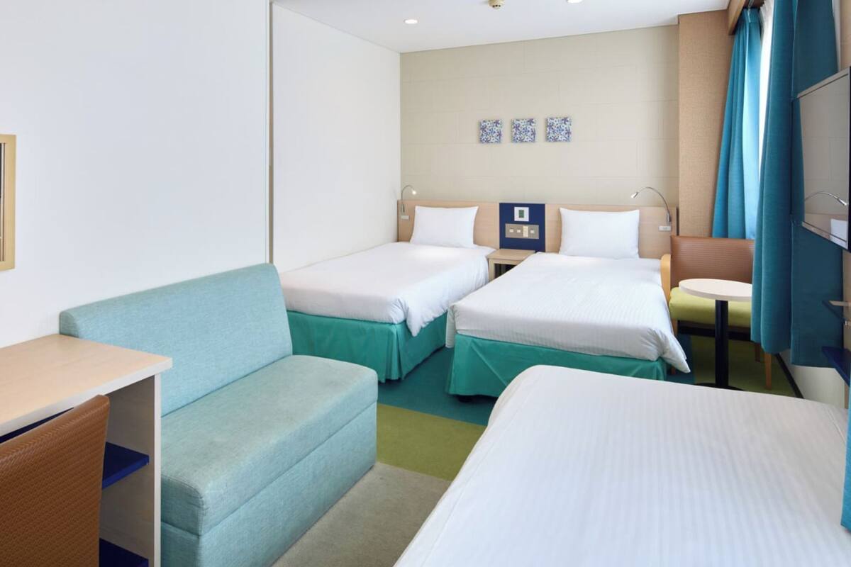 Une chambre d’hôtel avec deux lits, un bureau, un canapé, une télévision et un panneau de commande fixé au mur.
