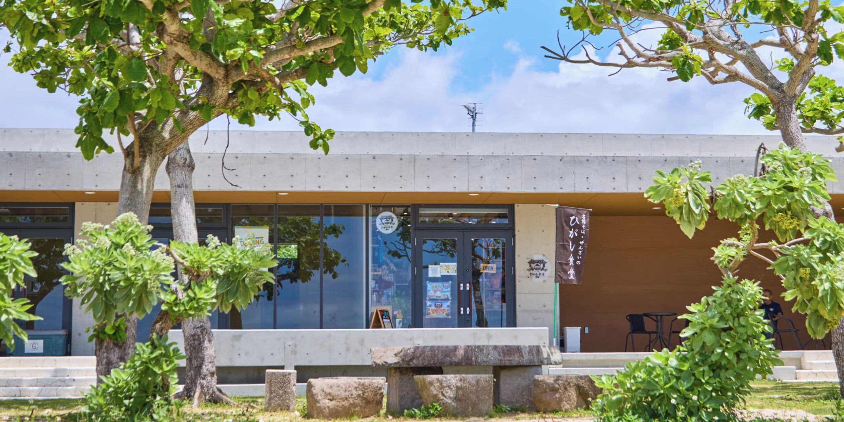 A modern building with a glass entrance, outdoor seating, and a stone bench.