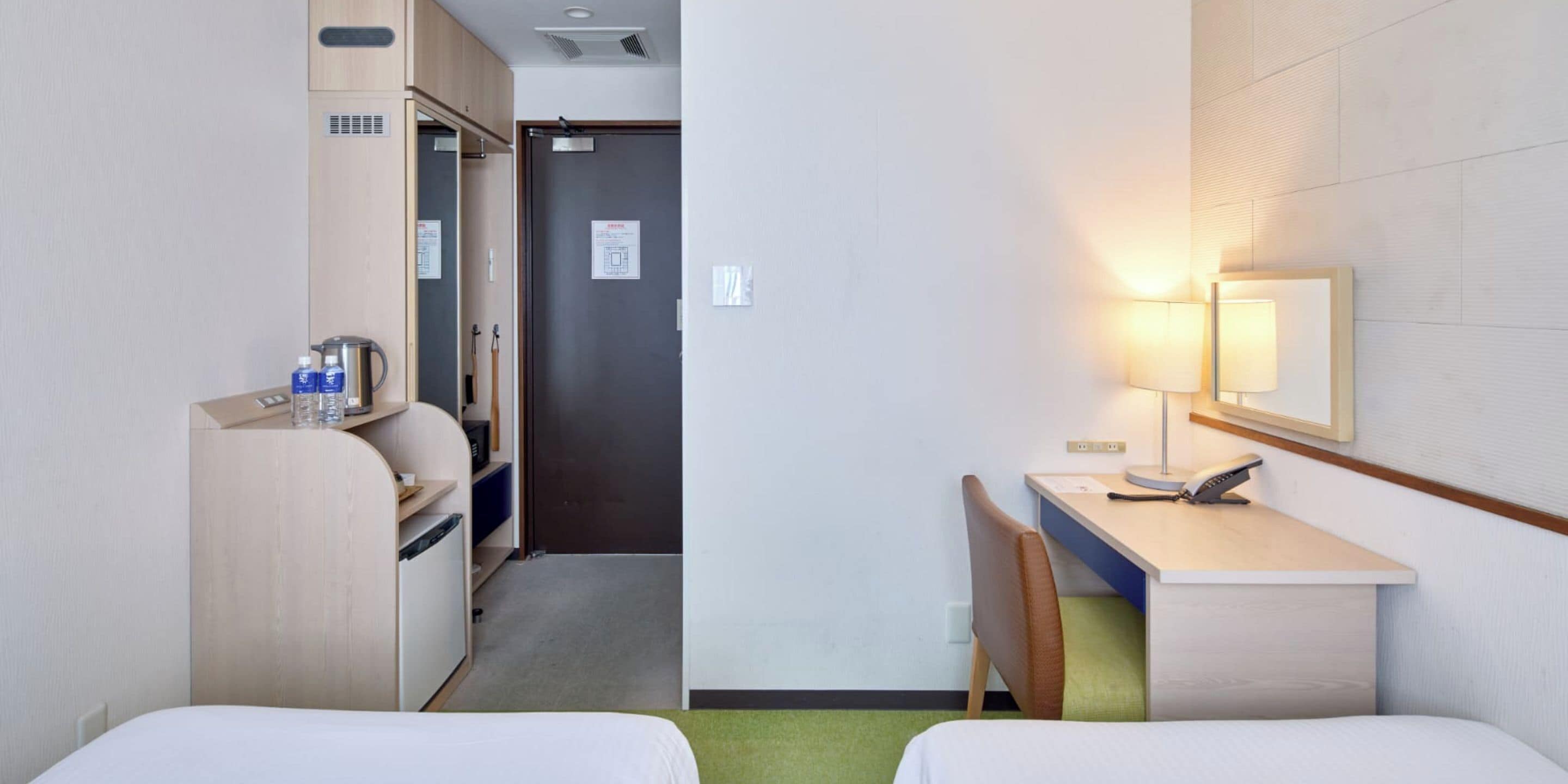 A hotel room with two beds, a desk with a chair, a desk lamp, a telephone, and a microwave.