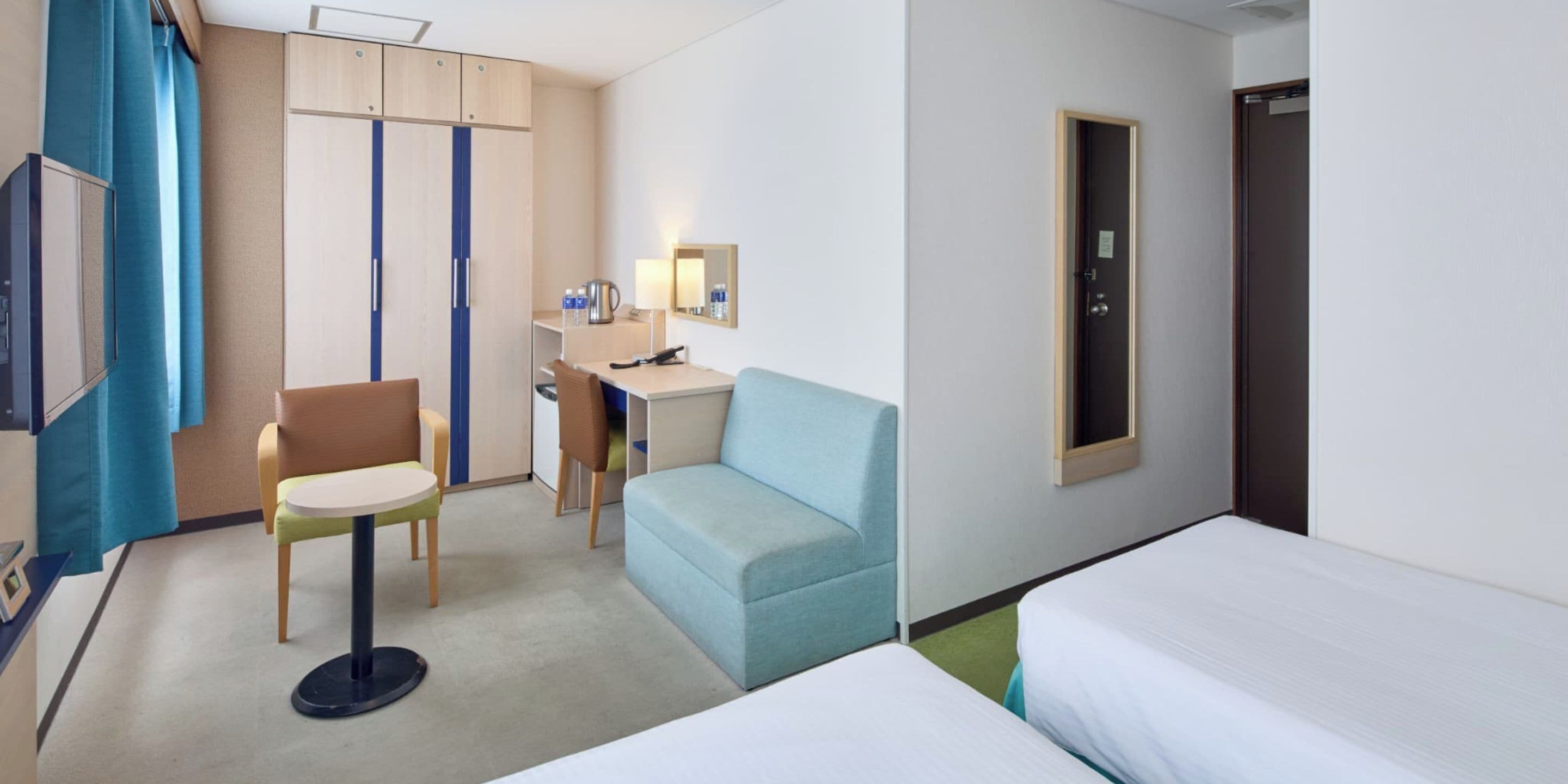 Una habitación de hotel con escritorio, una silla, sofá, dos camas, armario y espejo.