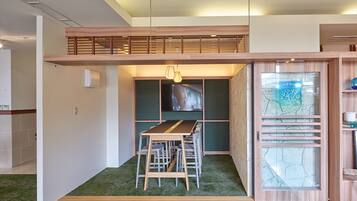 A modern interior with a dining area featuring a wooden table and chairs, a green carpet, and a view through a glass partition.