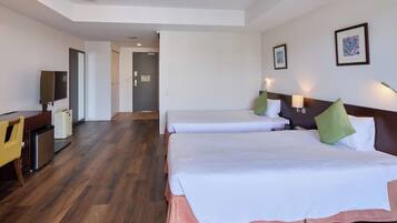Habitación de hotel con dos camas, un escritorio, una silla, un refrigerador pequeño y una puerta que conduce a otra habitación.