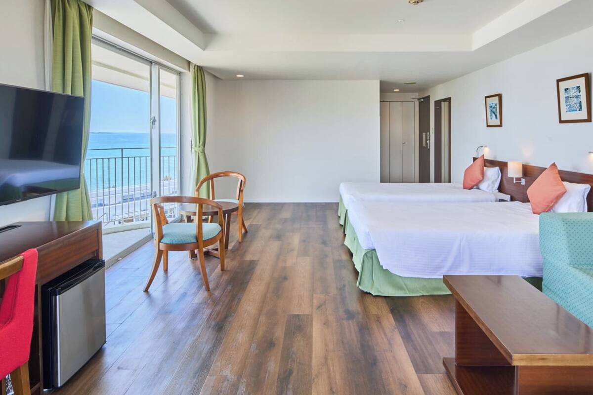 Une chambre d’hôtel équipée d’une télévision, de deux lits, d’un bureau, d’une chaise, d’un canapé et d’un balcon avec vue.