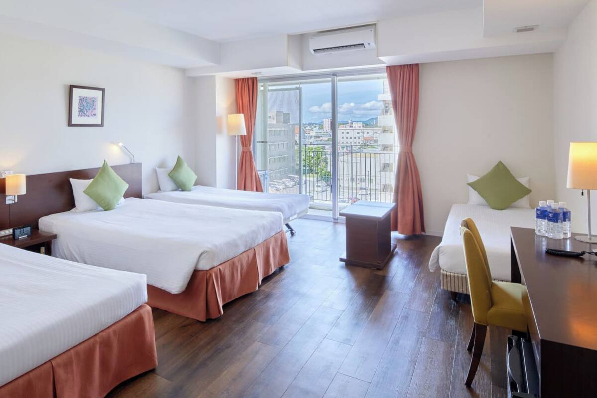 Une chambre d’hôtel avec trois lits, un bureau, une chaise et une vue sur la ville.