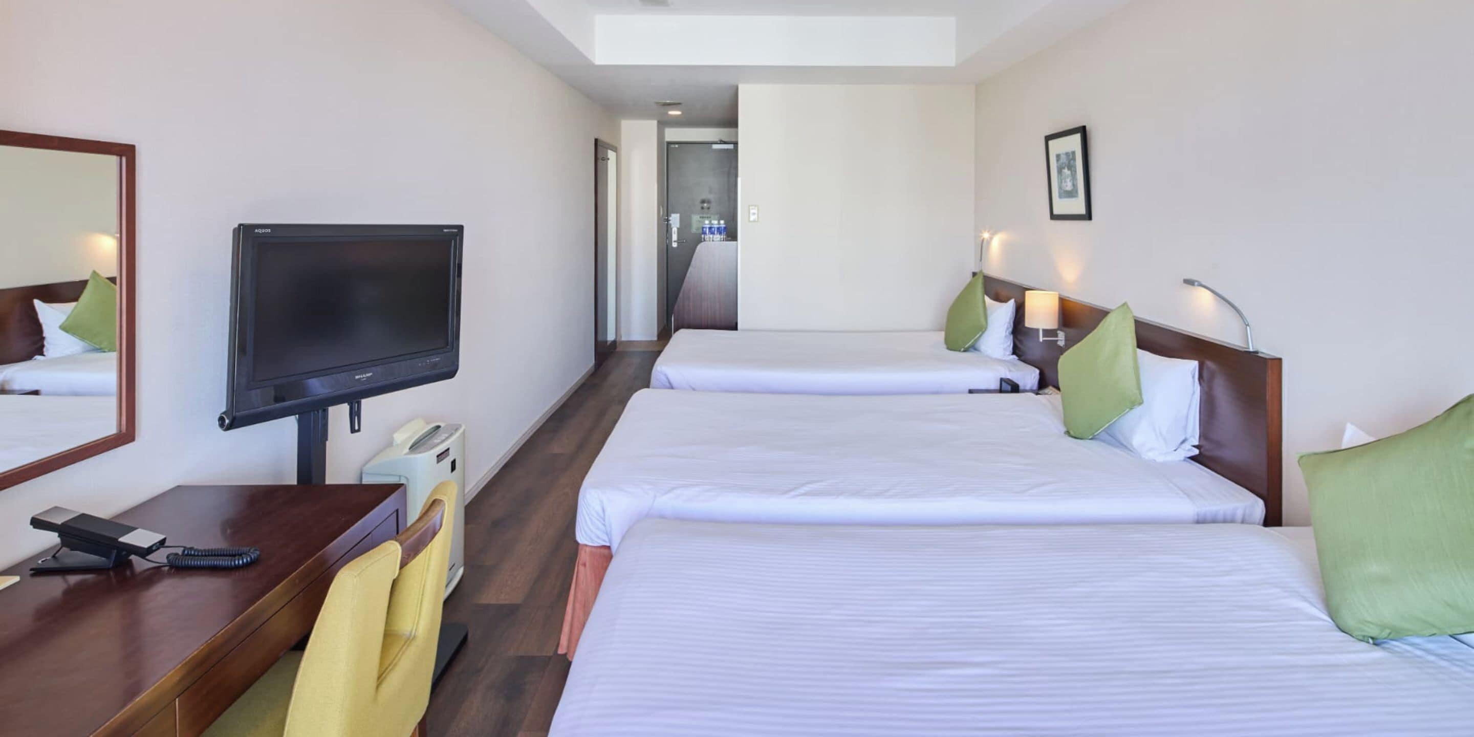 A hotel room with two beds, a TV, a desk with a phone, and a chair.