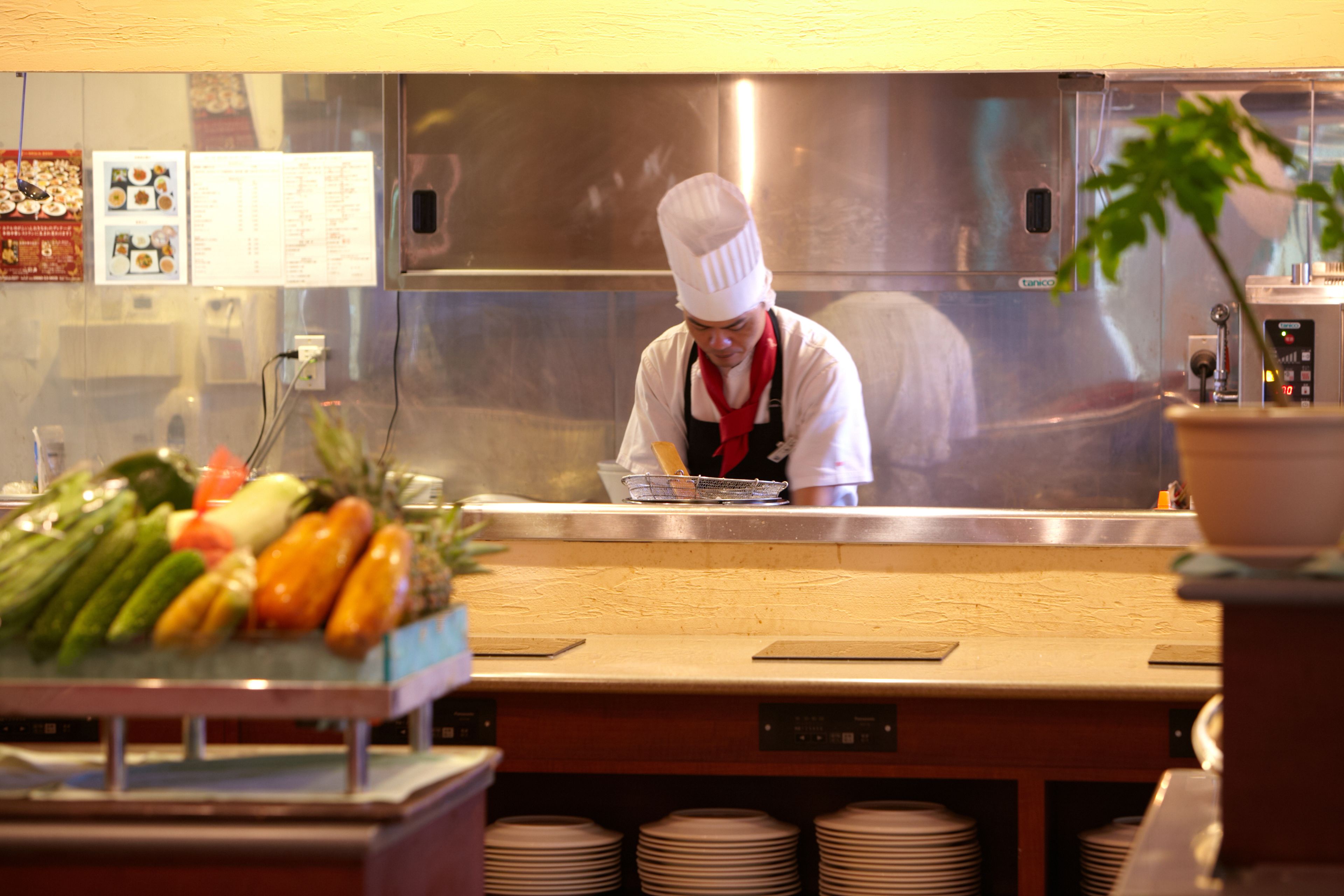 A chef in a professional kitchen with stainless steel appliances and a variety of fresh vegetables on the counter.