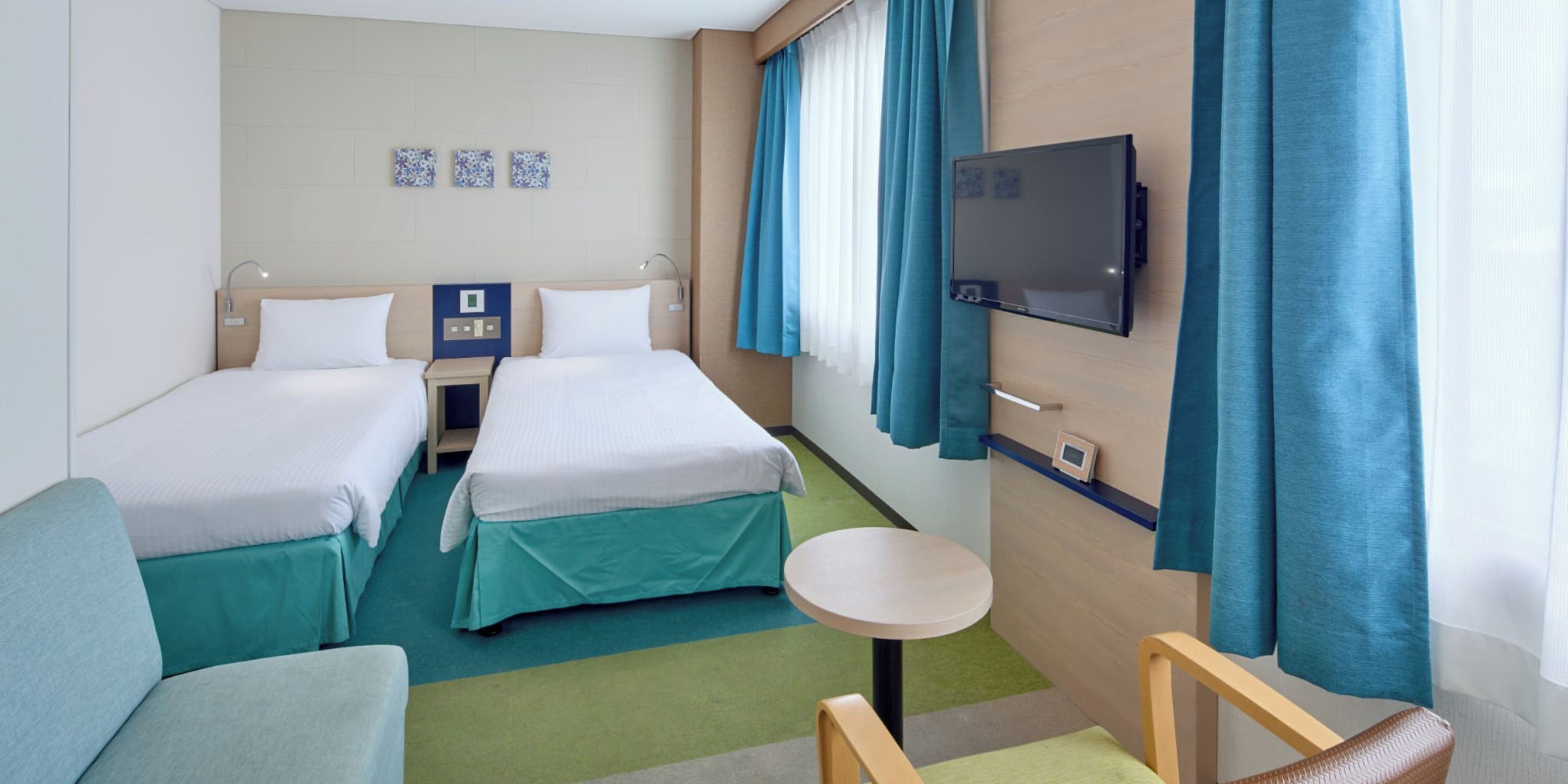 Ein Hotelzimmer mit zwei Betten, einem Fernseher, einem kleinen Tisch und einem Sofa.