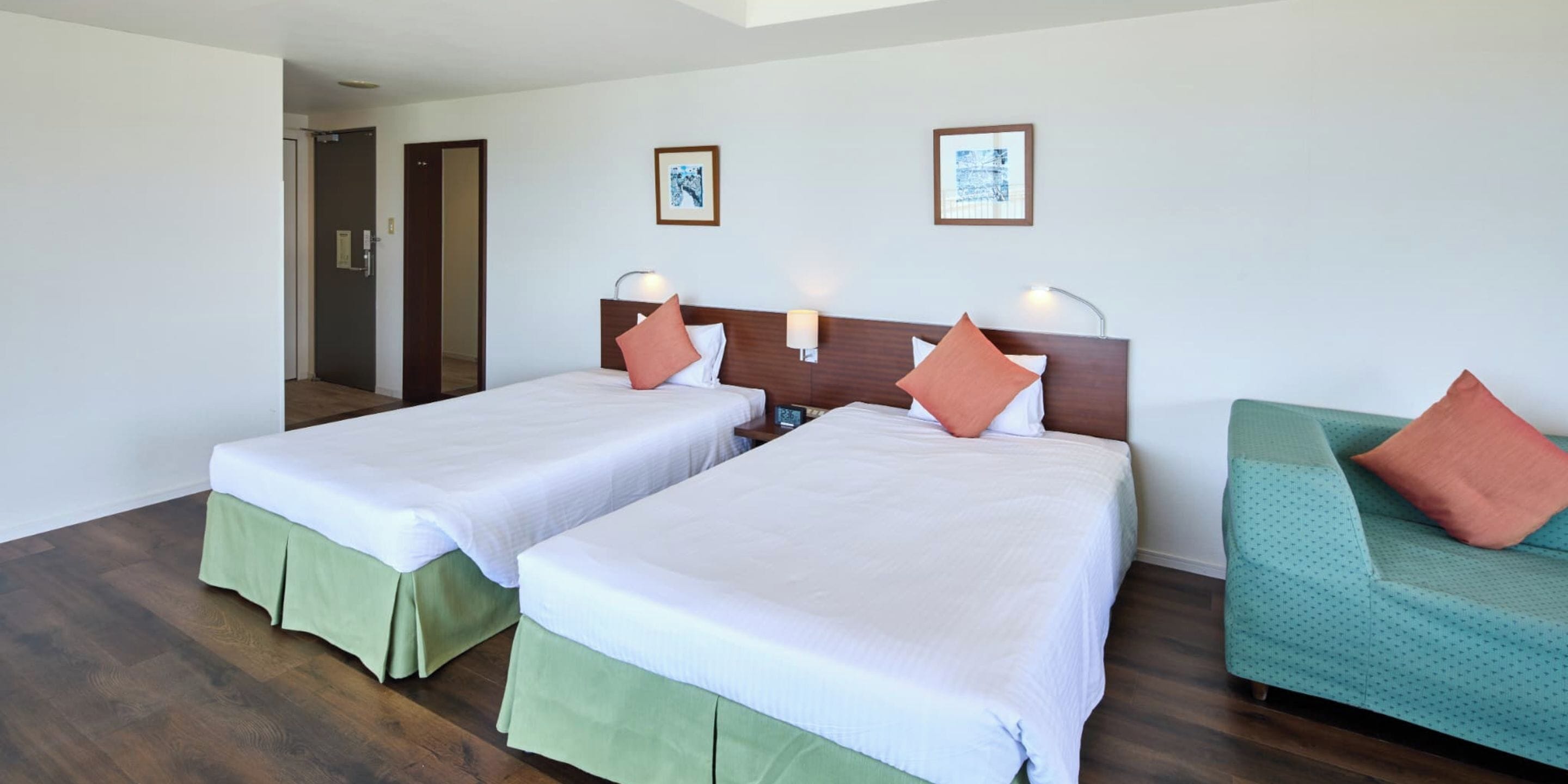 A hotel room with two beds, a green sofa, and two wall-mounted lamps.