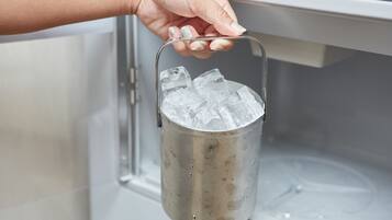 Una mano sostiene un recipiente metálico con cubitos de hielo, colocado dentro de un congelador.