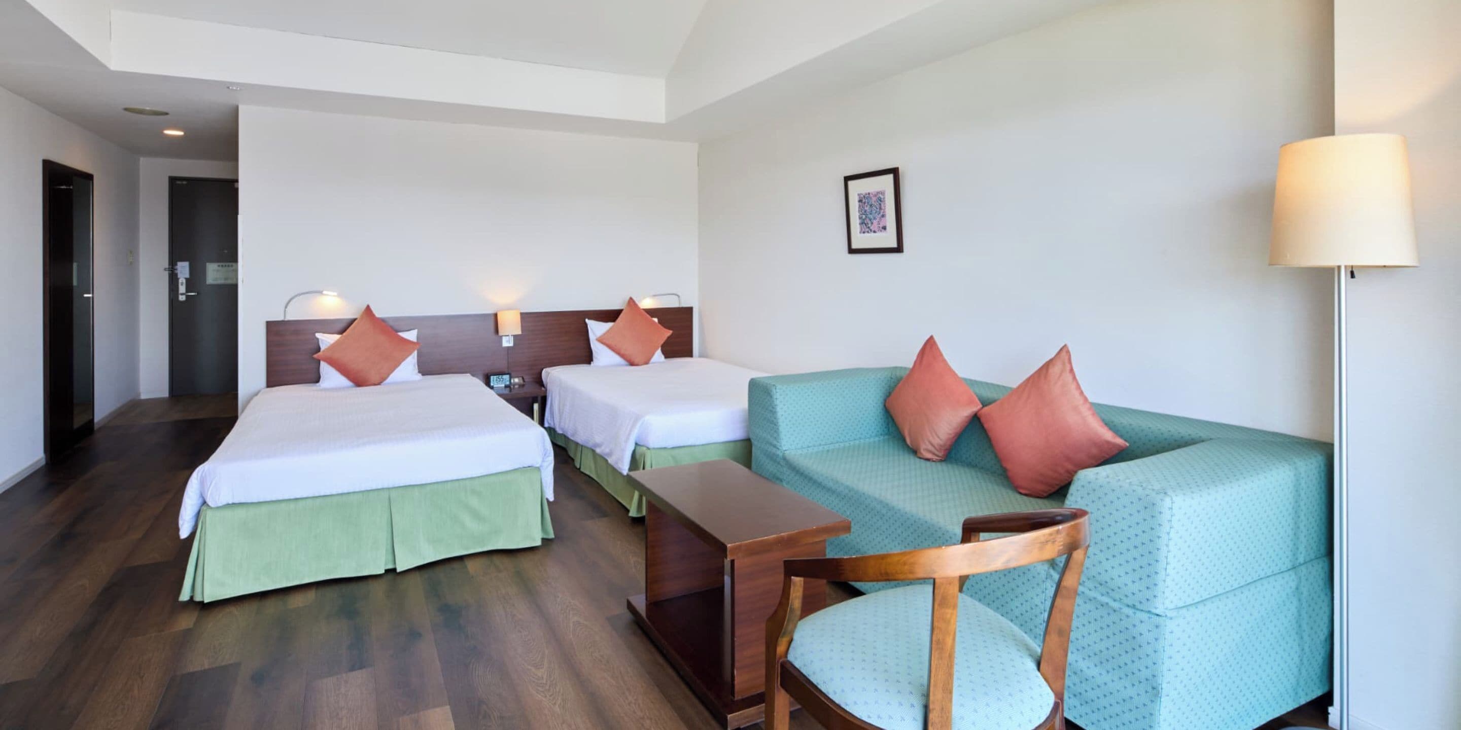 Een hotelkamer met twee bedden, een bank, een houten stoel, een kleine tafel en een lamp.
