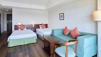 Een hotelkamer met twee bedden, een bank, een houten stoel, een kleine tafel en een lamp.