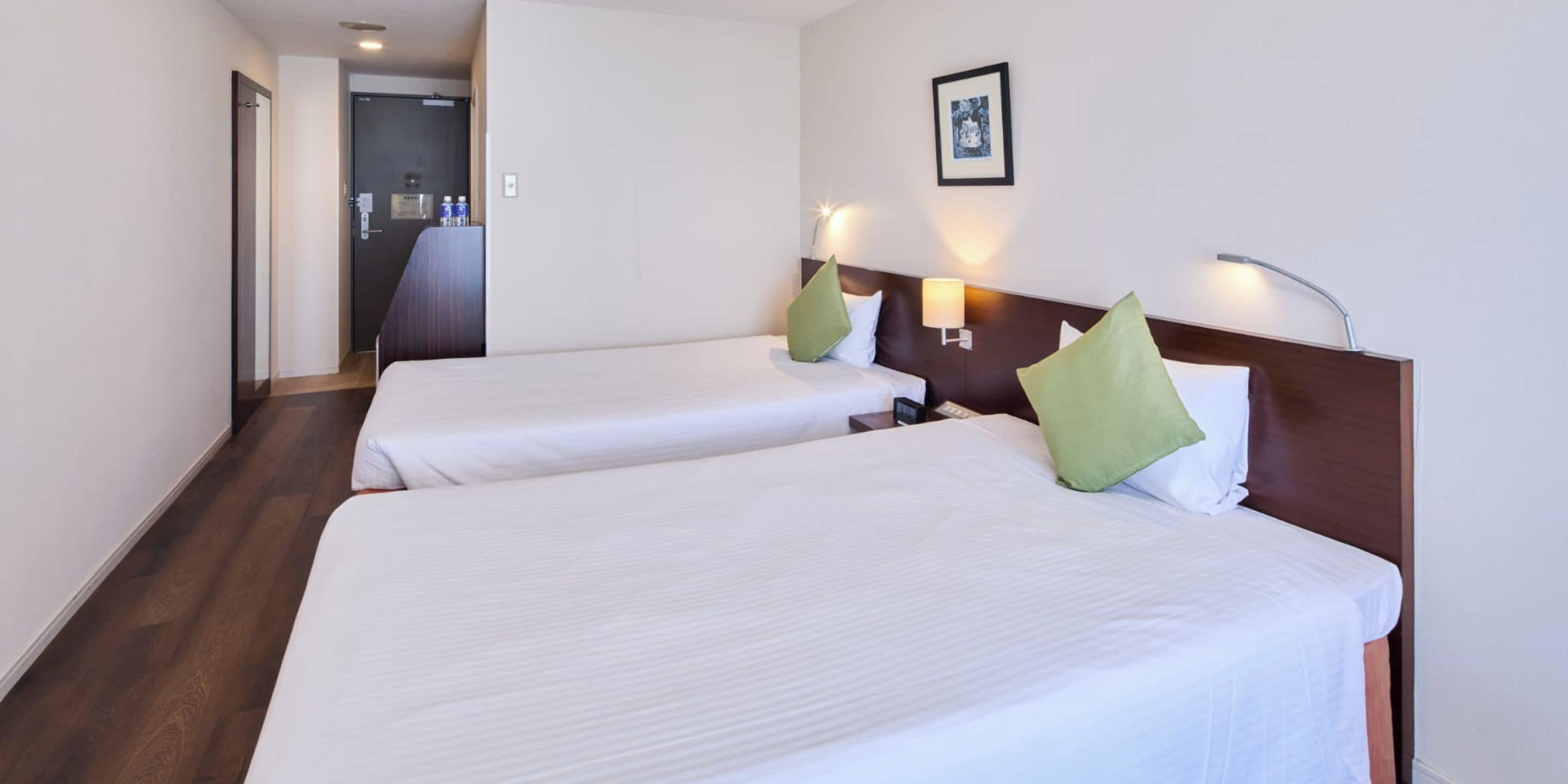 A hotel room with two beds, a desk, and a framed picture on the wall.