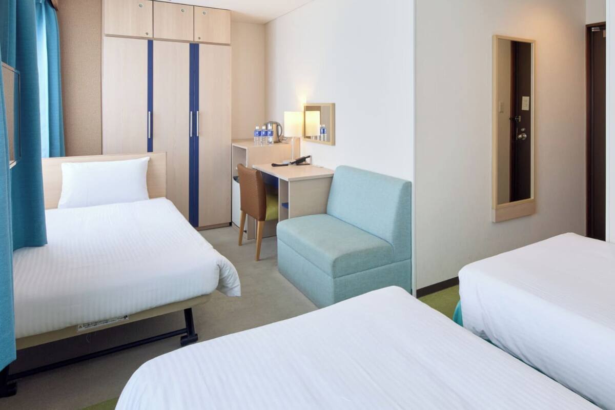 Une chambre d’hôtel avec deux lits, un bureau, une chaise, une armoire et un miroir.