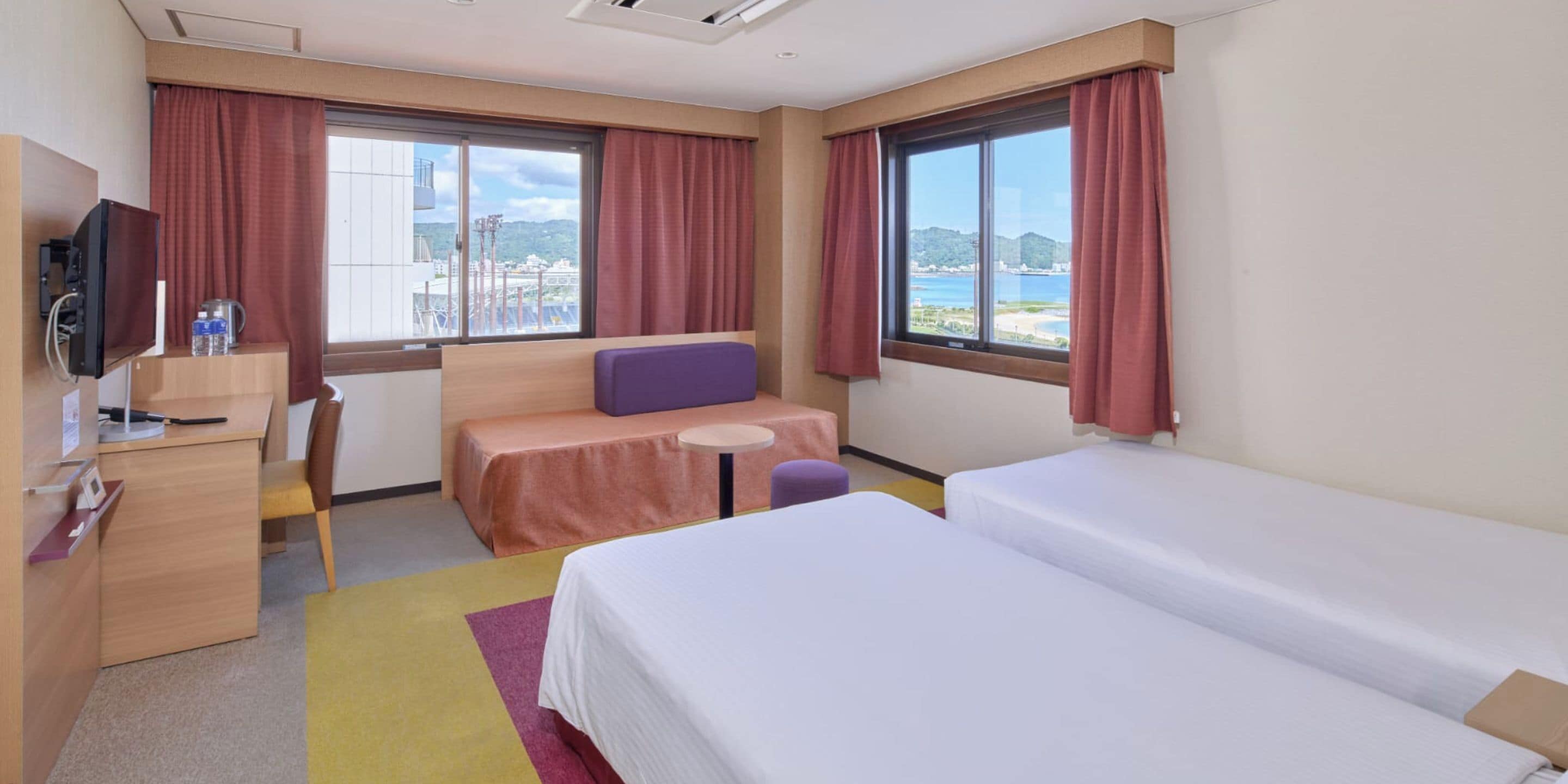 Habitación de hotel con cama, escritorio, silla, una mesita y televisor.