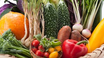 A variety of fresh vegetables and fruits, including broccoli, tomatoes, bell peppers, and carrots, arranged in a basket.