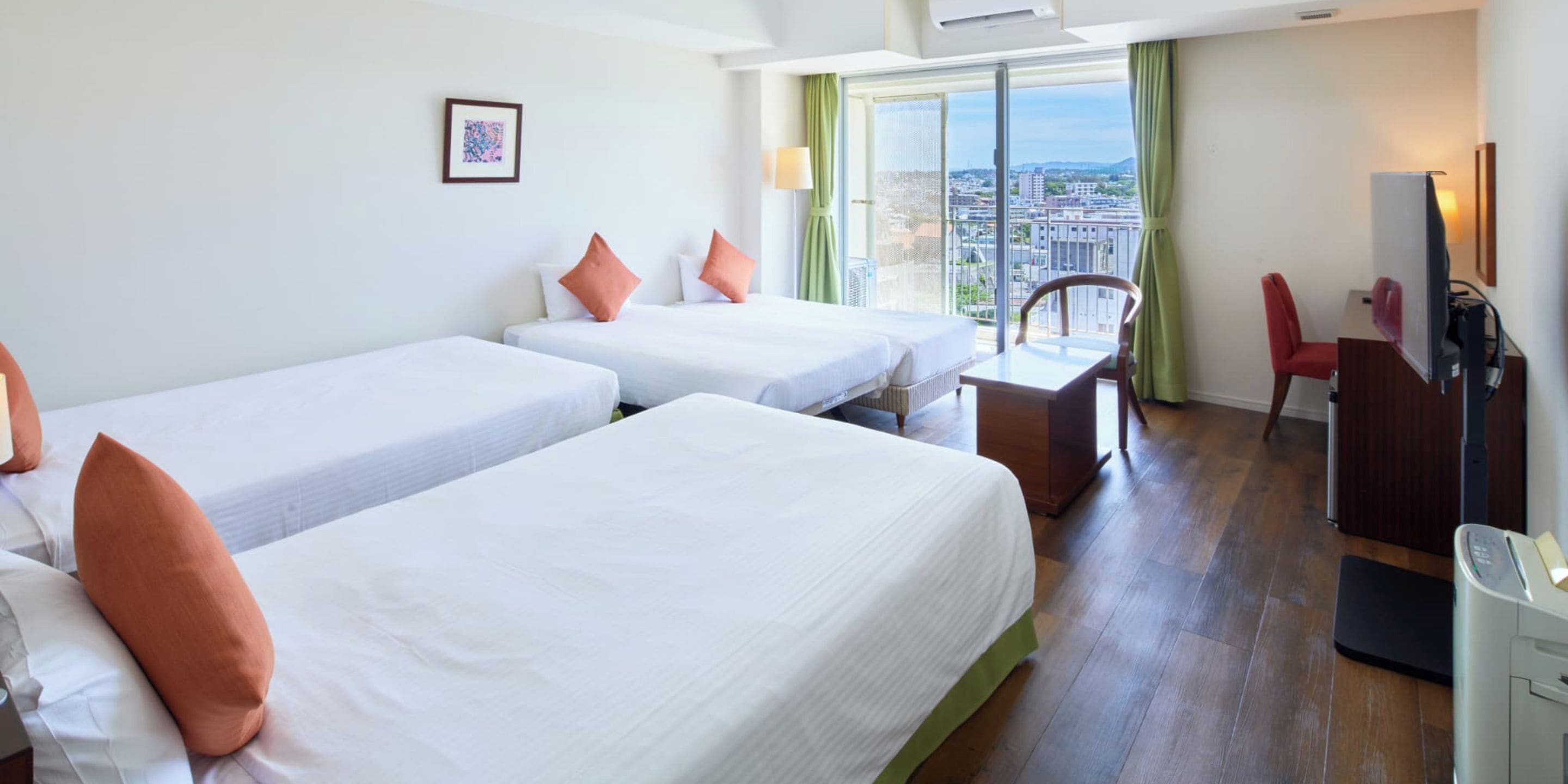 A hotel room with two beds, a desk, a chair, a TV, and a balcony with a city view.