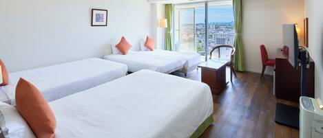A hotel room with two beds, a desk, a chair, a TV, and a balcony with a city view.