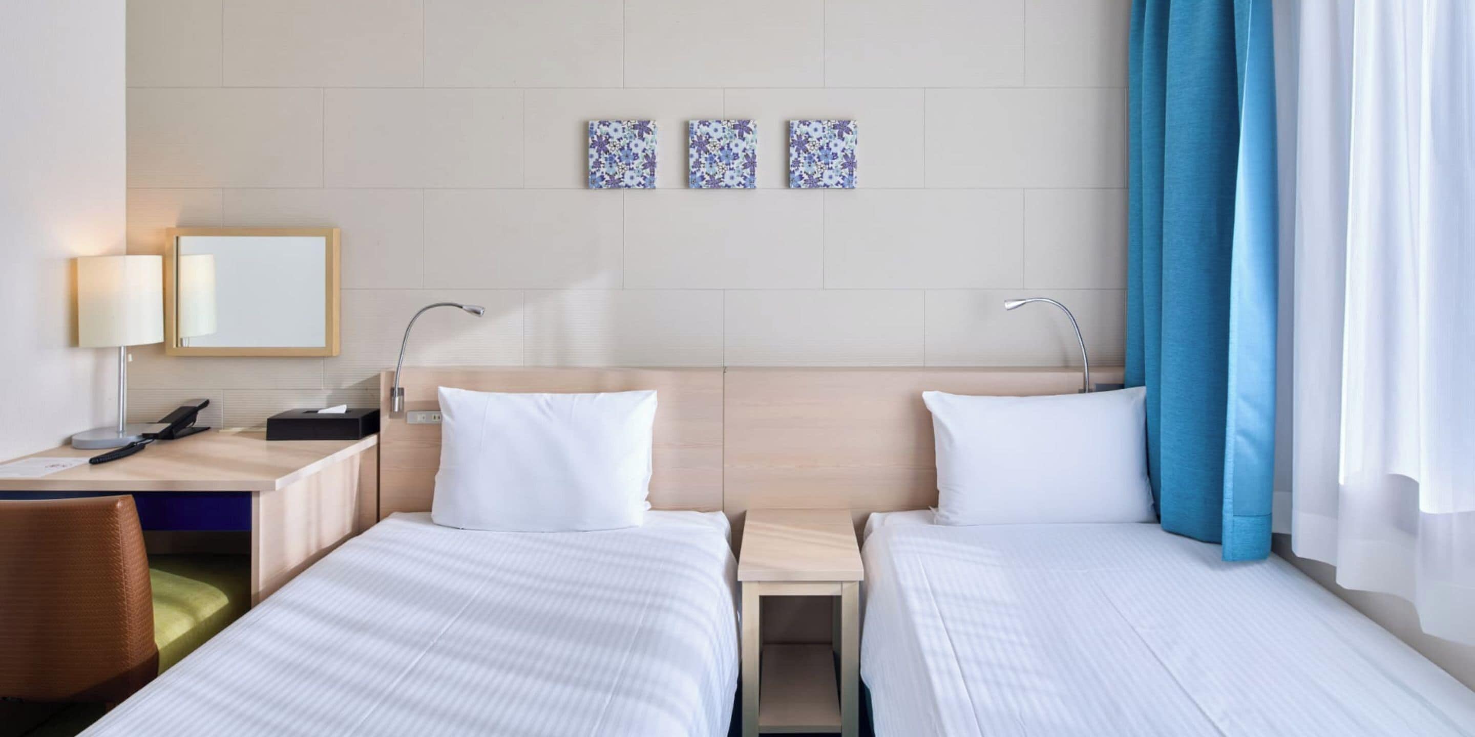 A hotel room with two beds, a desk with a lamp, a phone, and a chair.