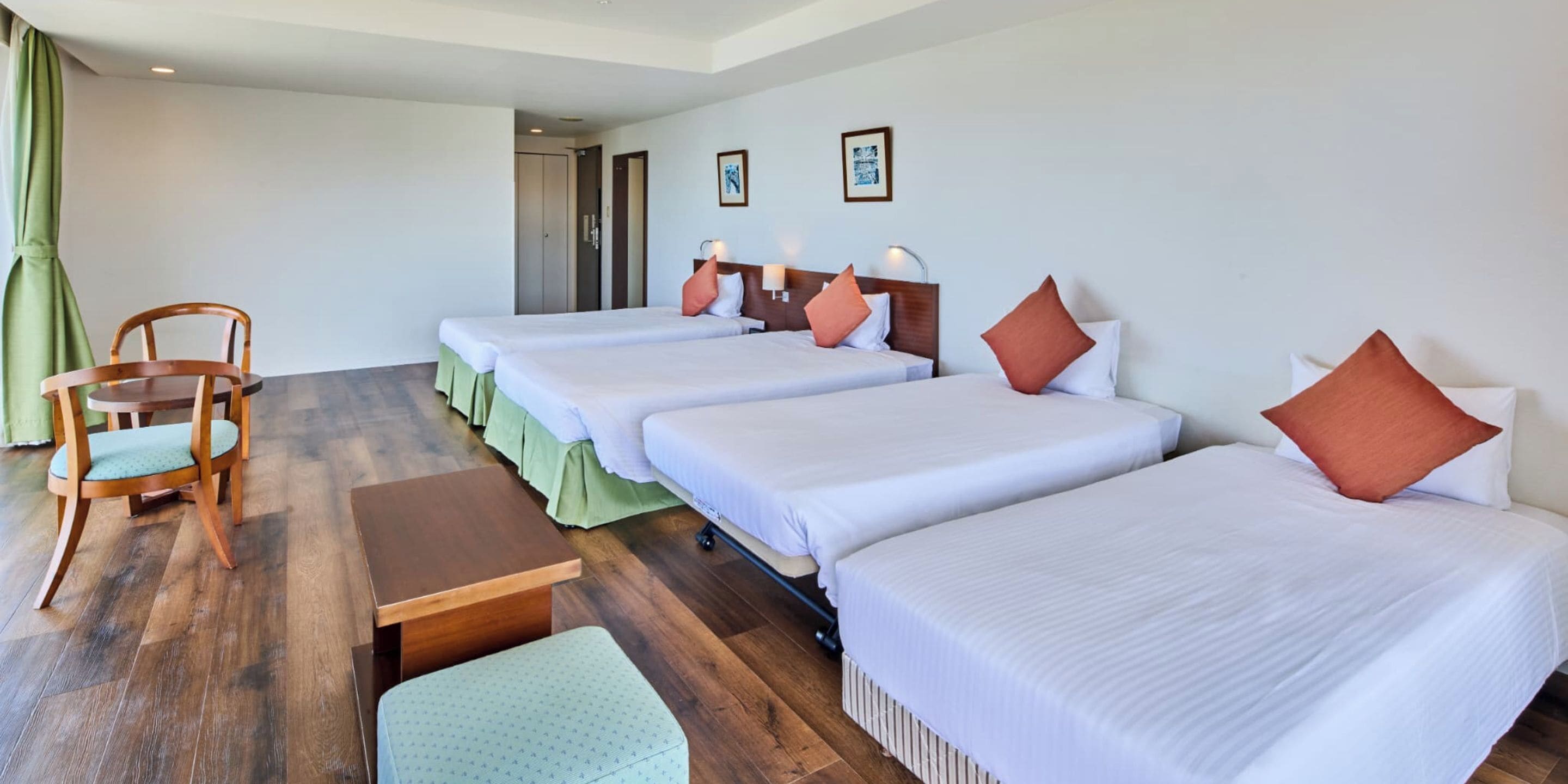 A hotel room with four single beds, a wooden chair, a small table, and a door leading to another room.