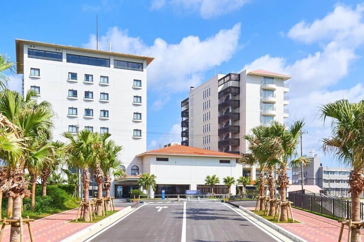 Un hotel moderno con un patio central, palmeras y cielo despejado.