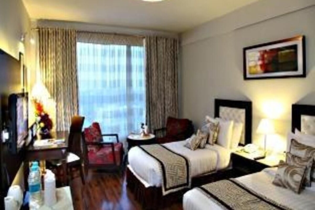 A hotel room with two beds, a desk, a chair, and a large window with curtains.