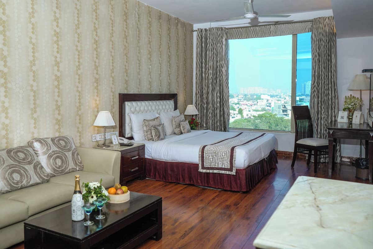 Une chambre d’hôtel comprenant un lit, un canapé, un bureau, une chaise, une table basse et une fenêtre donnant sur la ville.