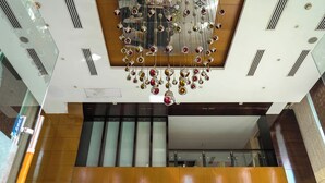 A modern interior with a decorative chandelier, a wooden panel with circular cutouts, and a glass railing. - TreeHouse Queens Pearl (Gurugram)