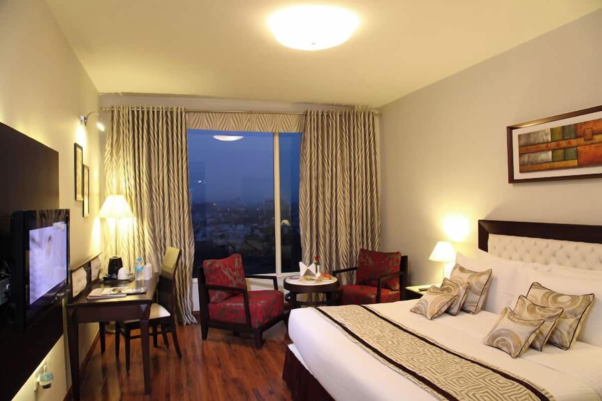 Une chambre d’hôtel avec un grand lit, deux fauteuils, une petite table, un téléviseur et une fenêtre avec des rideaux.