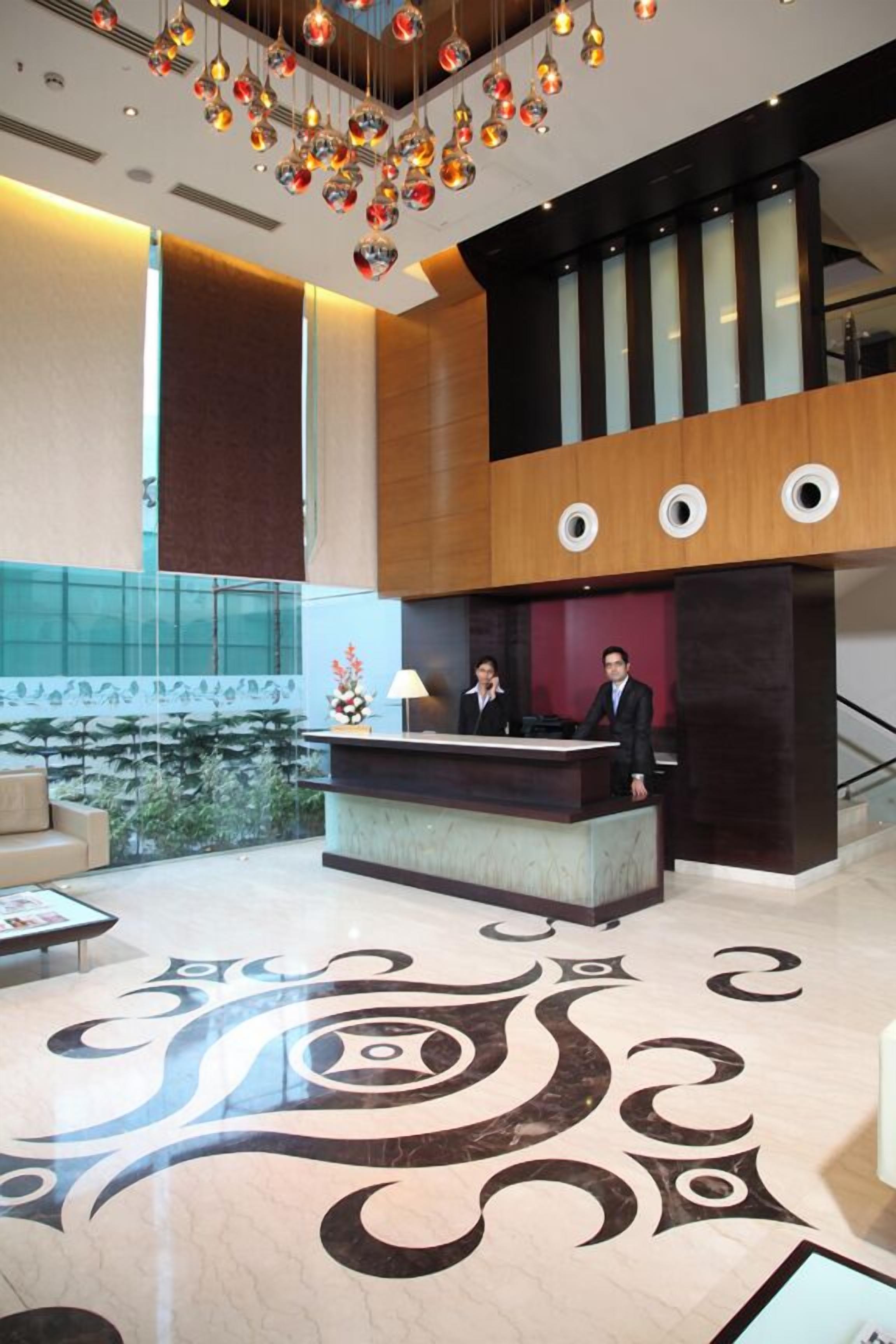 Vestíbulo de hotel con mostrador de recepción, dos empleados, techo decorativo y un amplio ventanal con vistas.