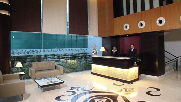 A hotel lobby with a reception desk, a sofa, a coffee table, and a decorative wall with a mural. - TreeHouse Queens Pearl (Gurugram)