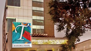 A hotel with a prominent 'T' logo, a glass facade, and a well-lit entrance. - TreeHouse Queens Pearl (Gurugram)