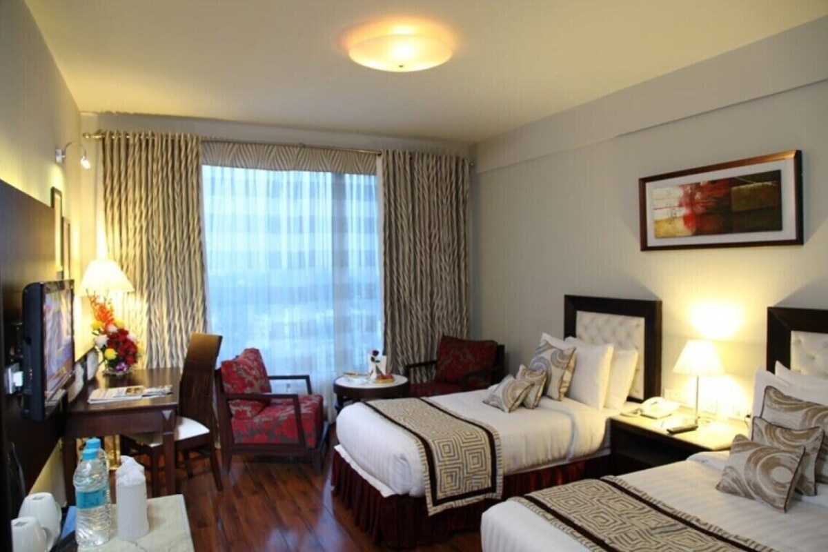 A hotel room with two beds, a desk, a chair, a television, and a window with curtains.