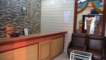 A reception area with a wooden counter, a seating area with brown leather chairs, and a tiled wall with a clock.