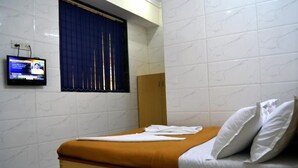 A hotel room with a bed, a television mounted on the wall, and a window with blue curtains. - Hotel New Deepak (Mumbai)