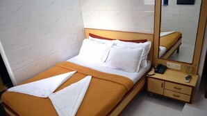 A neatly made bed with white and orange bedding, a bedside table with a phone, and a mirror reflecting the room. - Hotel New Deepak (Mumbai)