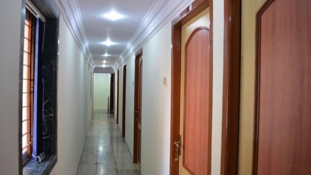 A long, narrow hallway with wooden doors on one side and a window with blinds on the other. - Hotel New Deepak (Mumbai)