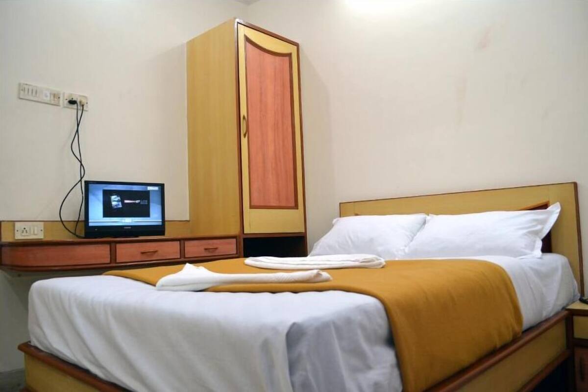 Una habitación de hotel con cama, armario, escritorio con computadora y toma de corriente.