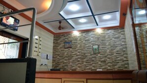A reception area with a tiled wall, a ceiling with recessed lighting, and a television mounted on the wall. - Hotel New Deepak (Mumbai)