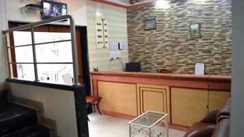 A reception area with a wooden counter, a glass table, a brown leather couch, and a staircase.