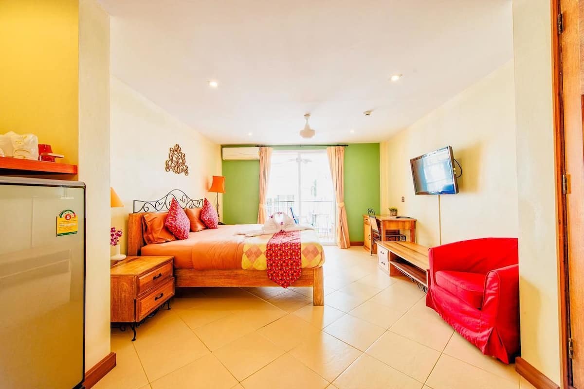 A bedroom with a bed, bedside table, lamp, TV, and a red chair.