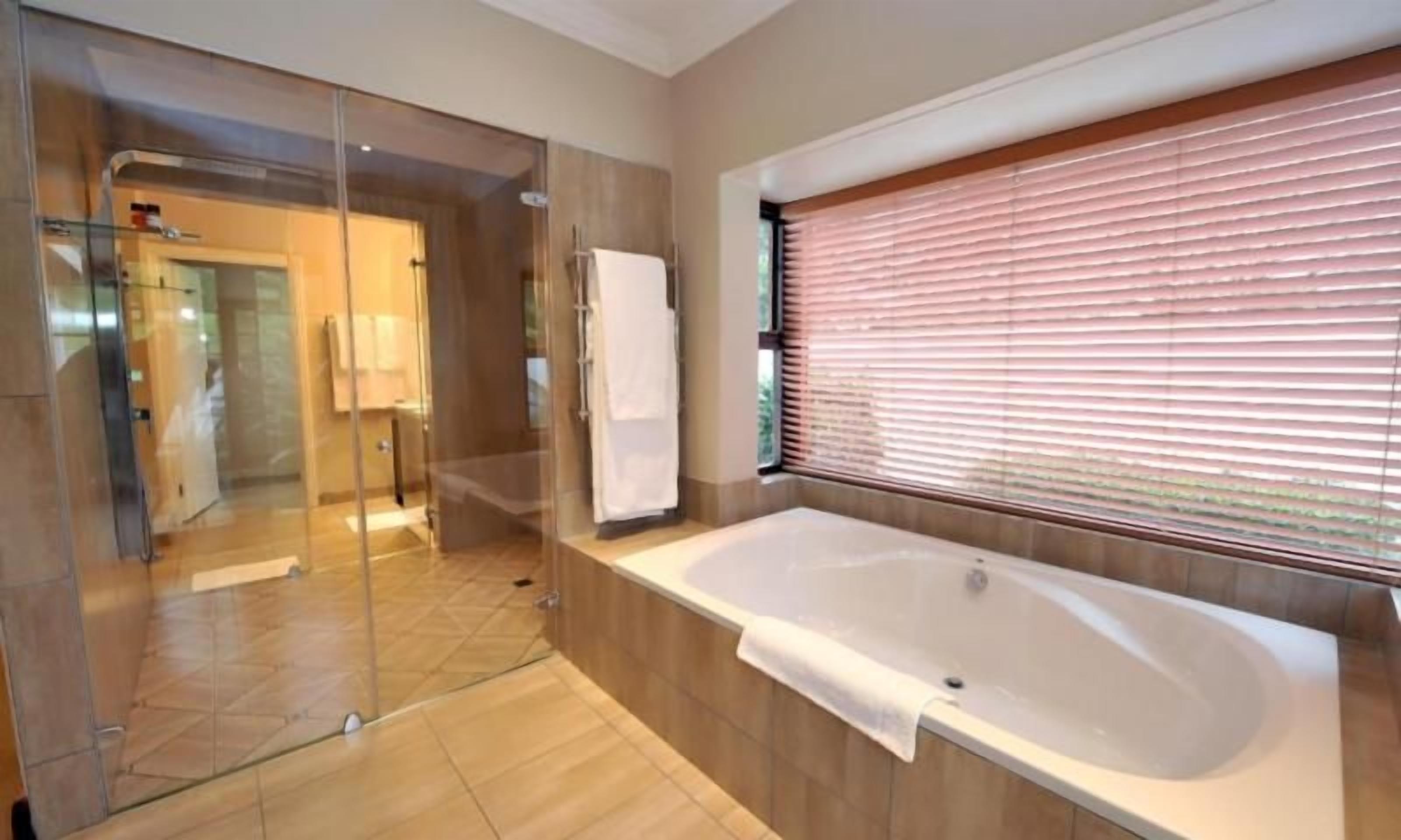 A modern bathroom with a glass shower enclosure, a large bathtub, and a window with blinds.