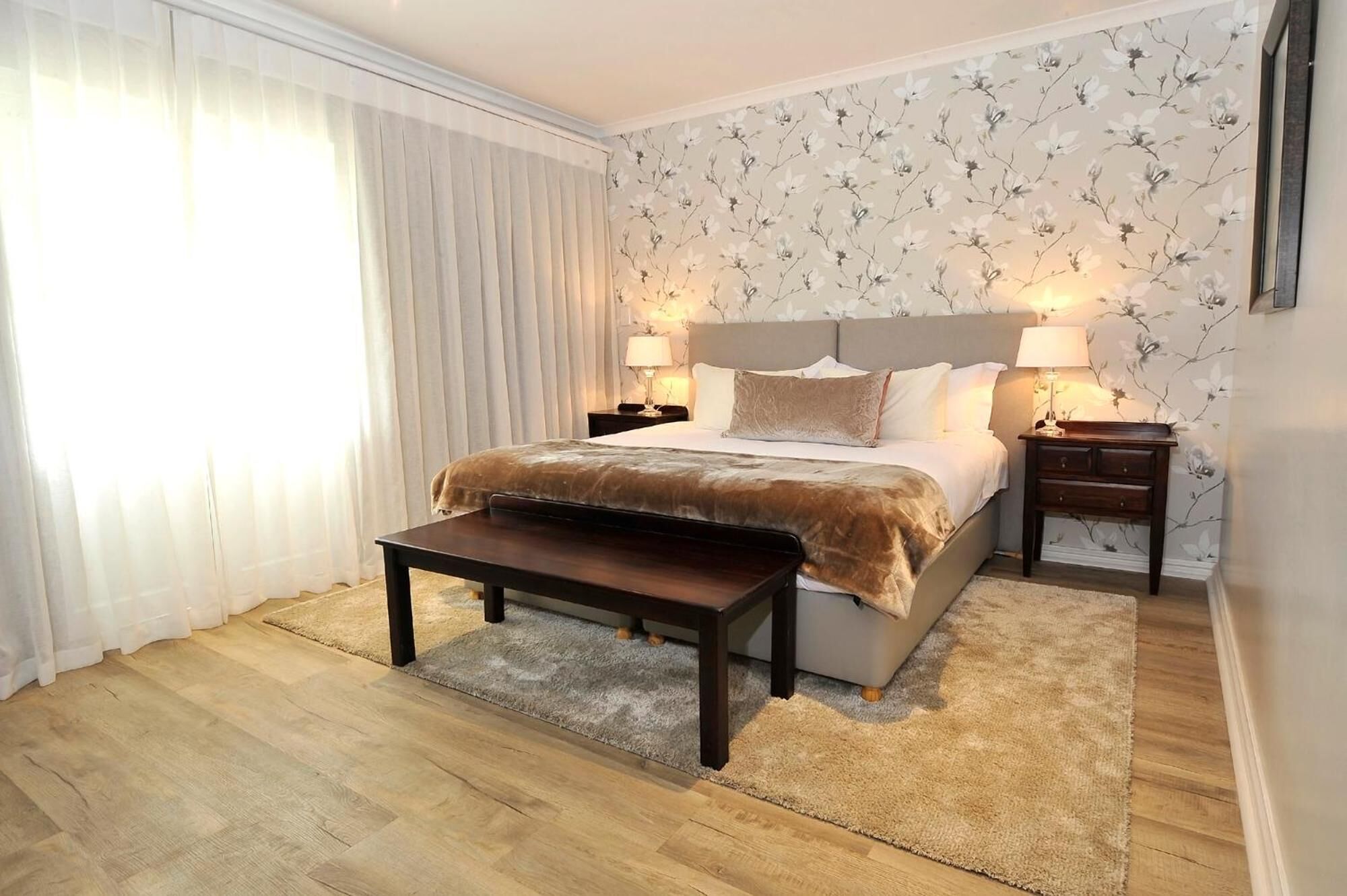 Une chambre à coucher avec un lit, des tables de chevet, une commode, un plancher en bois et une fenêtre avec des rideaux.