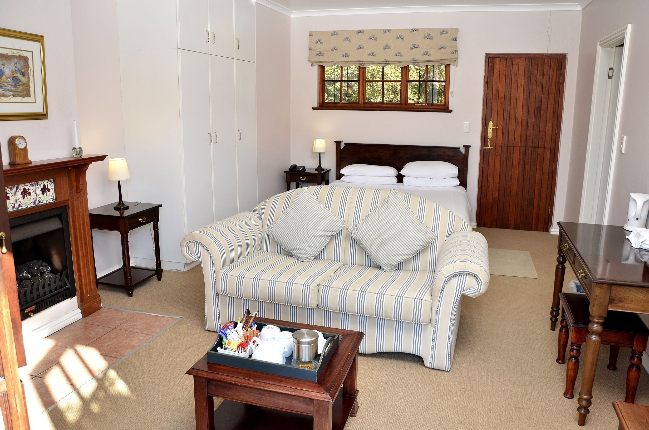 A hotel room with a bed, a striped sofa, a wooden coffee table, a fireplace, and a window with a curtain.