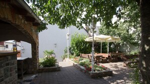 An outdoor patio with stone flooring, a wooden bench, and a table with a yellow umbrella. - Hotel Rhein-Mosel-View (Urbar)