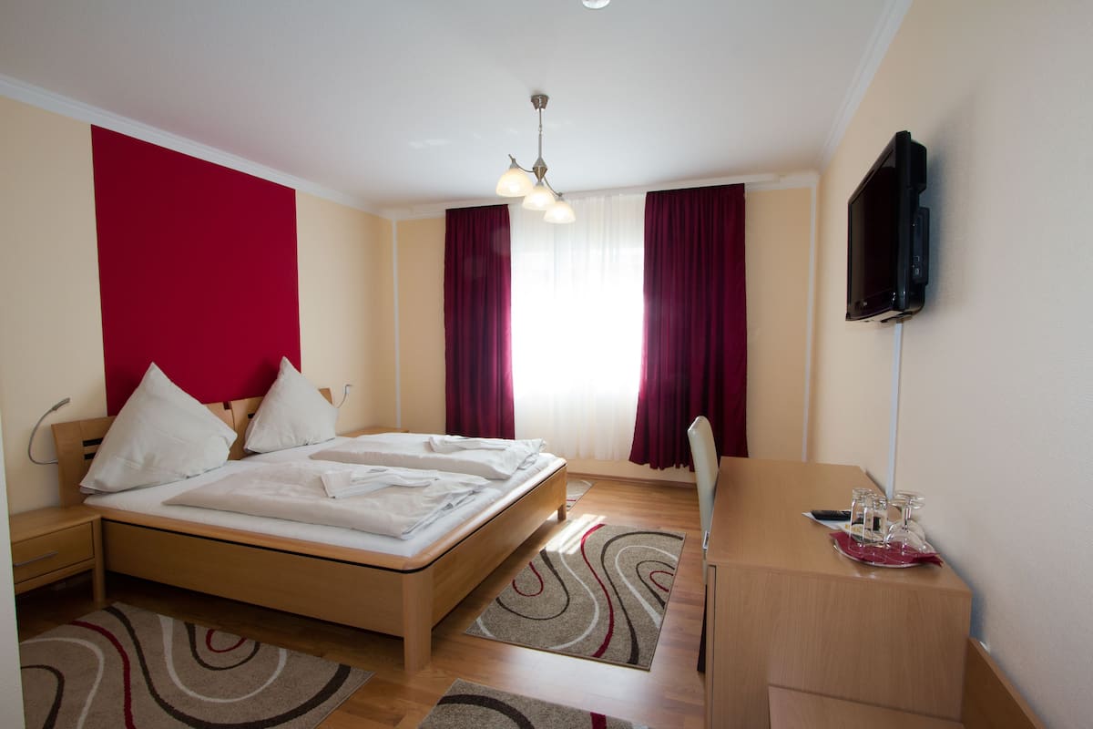 A hotel room with a bed, a desk, a television, and a window with curtains.