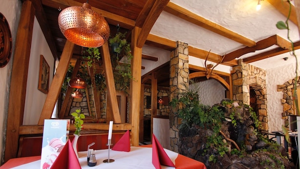 A restaurant interior with a stone wall, wooden beams, and hanging plants. - Hotel Rhein-Mosel-View (Urbar)